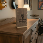 Personalized wooden urn on a buffet with guitars, and pictures hanging on the wall. Drum kit set up in the back corner of the room